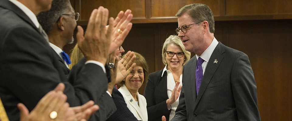 Dr. Cecil P. Staton, in a purple tie, greeted with applause by colleagues in a wood-paneled room